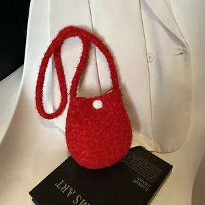 Mini sac seau chic en peluche rouge avec bouton à pois blancs sur fond de blazer blanc