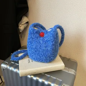 Sac seau chic en peluche bleu électrique avec pompon rouge sur une valise élégante
