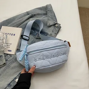Light blue quilted nylon chest bag with wave embroidery on casual denim background