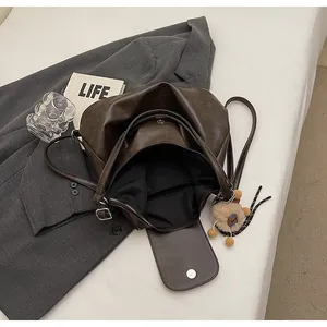 Detail view of brown tote bag with smooth texture, inner zipper pocket and plush ball charm