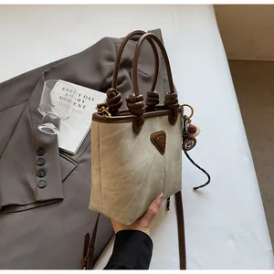 Detail of canvas tote bag featuring leather trim, knot handle, and metallic logo pendant