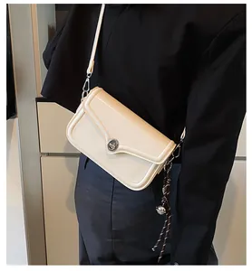 Detail of cream crossbody bag with silver twist lock and woven charm on a black suit
