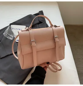 Pink vintage messenger bag with double buckle straps on a grey suit background