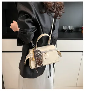 Detail of beige pillow bag with double zippers and decorative charms on a model