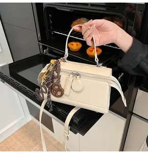 Detail of cream pillow bag featuring dual zippers and playful charms against a kitchen backdrop