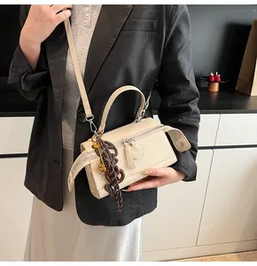 Detail of cream leather rectangular satchel with woven charm and detachable strap