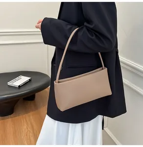 Close-up of minimalist apricot baguette bag worn by a model in a modern interior