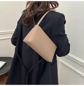 Detailed back view of a minimalist beige baguette shoulder bag worn with a black blazer