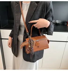 Detailed view of a brown cylinder bag featuring twin zippers and stylish pendant charms