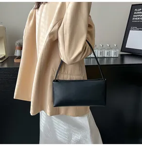 Minimalist black leather baguette bag on model in a modern chic indoor setting