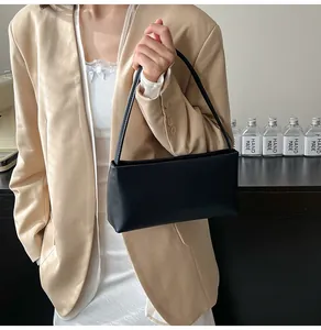 Detail of minimalist black baguette bag held by model wearing a beige blazer