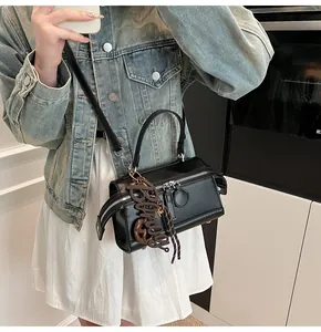 Close-up of black crossbody pillow bag featuring a stylish brown letter charm and metal zip