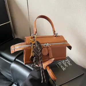 Brown leather doctor bag with dual zippers and decorative charms on a stylish background