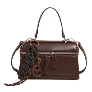 Dark brown leather top handle crossbody bag with dual zippers and decorative lettering pendant