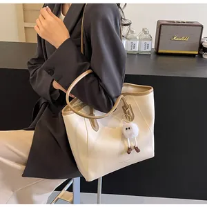 Detailed view of beige tote bag with brown trim and plush charm worn on shoulder