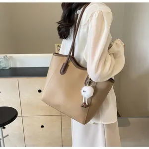 Lifestyle shot of a stylish khaki tote bag with dark brown straps and a white pompom charm