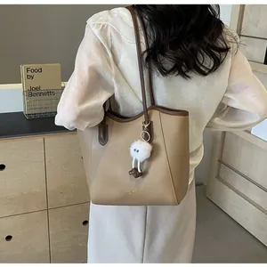 Detail of khaki tote bag with dark brown contrast straps and a plush white doll charm