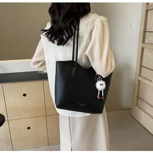 Detail of black faux leather tote bag with gold lettering and cute plush doll pendant