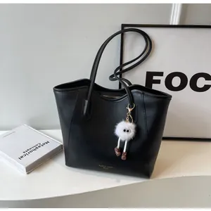 Detail of black leather tote bag with a white plush doll charm and bottom text branding