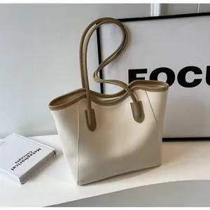Detail of minimalist cream tote bag with khaki piping, zipper closure, and slim handles