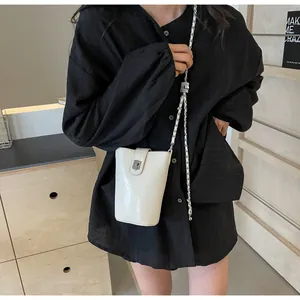 Close-up of a white glossy bucket bag with silver chain strap shown on a model