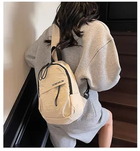 Beige Nylon-Umhängetasche an einem Model in einem modernen Treppenhaus getragen