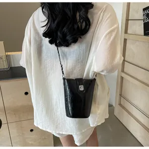 Detail of a shiny black bucket bag with silver chain strap worn over a white linen shirt