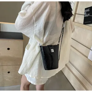 Detail of black glossy bucket bag with silver twist lock and chain shoulder strap