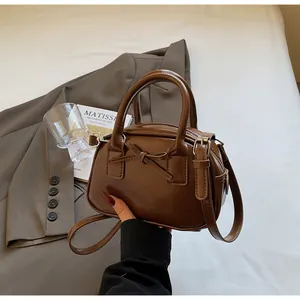 Detail of a dark brown mini Boston bag featuring a stylish bow and smooth faux leather finish
