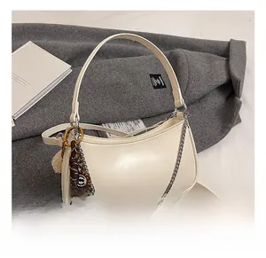 Close-up of cream crescent bag with silver chain, woven charm, and brand logo detail