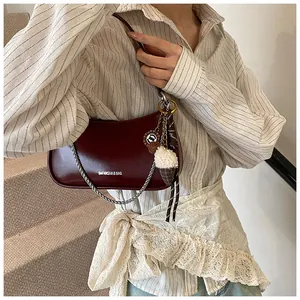 Detail of burgundy half-moon bag featuring silver chain, plush charm and ribbon decor