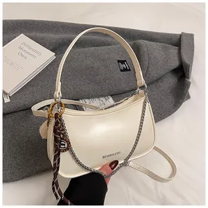 Detail view of cream saddle bag featuring metallic chain, logo print and plush charm