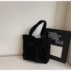 Detail of black corduroy tote bag showing front double pockets and ribbed fabric texture