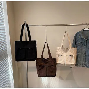 Detailed close-up of corduroy tote bags in black, brown, and cream with front dual pockets