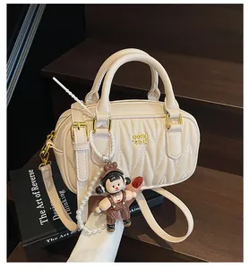 Detalle del bolso plisado beige con herrajes dorados y colgante de muñeca con perlas