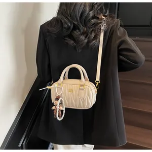 Detalle del bolso de hombro plisado crema con cremallera dorada y colgante de perlas