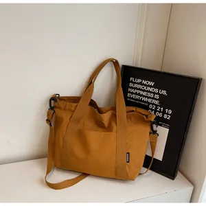 Detail van mosterdgele canvas draagtas met verstelbare riem en wit geweven label