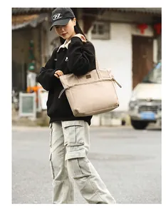 Dettaglio di una grande borsa tote in nylon beige con logo in pelle e coulisse laterale