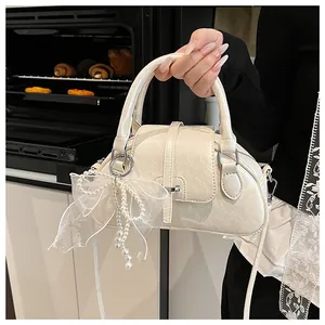 Close-up of cream Boston bag with a pearl mesh bow pendant and fine leather texture