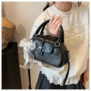 Detail of glossy black Boston bag featuring lace bow and pearl chain pendant decoration