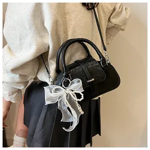 Detail of black leather pillow bag with white lace bow and pearl chain charm