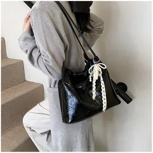 Detail of black glossy tote bag with lace pearl bow charm and shoulder strap texture