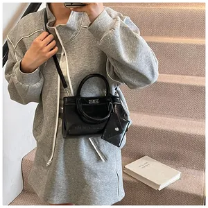 Détail d'un sac à main noir brillant avec fermoir rotatif en métal et bandoulière amovible