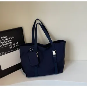 Detail of navy blue nylon tote bag with wide straps, buckle, and matching small pouch