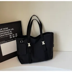 Detail of black nylon tote bag featuring silver buckles and detachable small pouch accessory