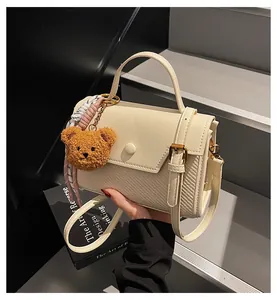 Close-up of cream square handbag with woven texture and cute plush bear charm decoration
