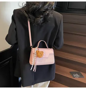Detailed back view of pink crossbody bag with teddy bear charm on wooden stairs