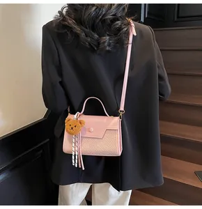 Detail of pink leather handbag with teddy bear charm shown on a shoulder strap