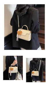 Detail view of cream woven crossbody bag featuring bear charm and checkered scarf accent