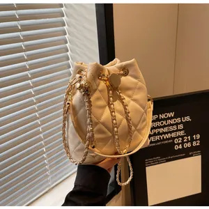 Close-up of quilted cream bucket bag with gold ball clasp and metal chain strap